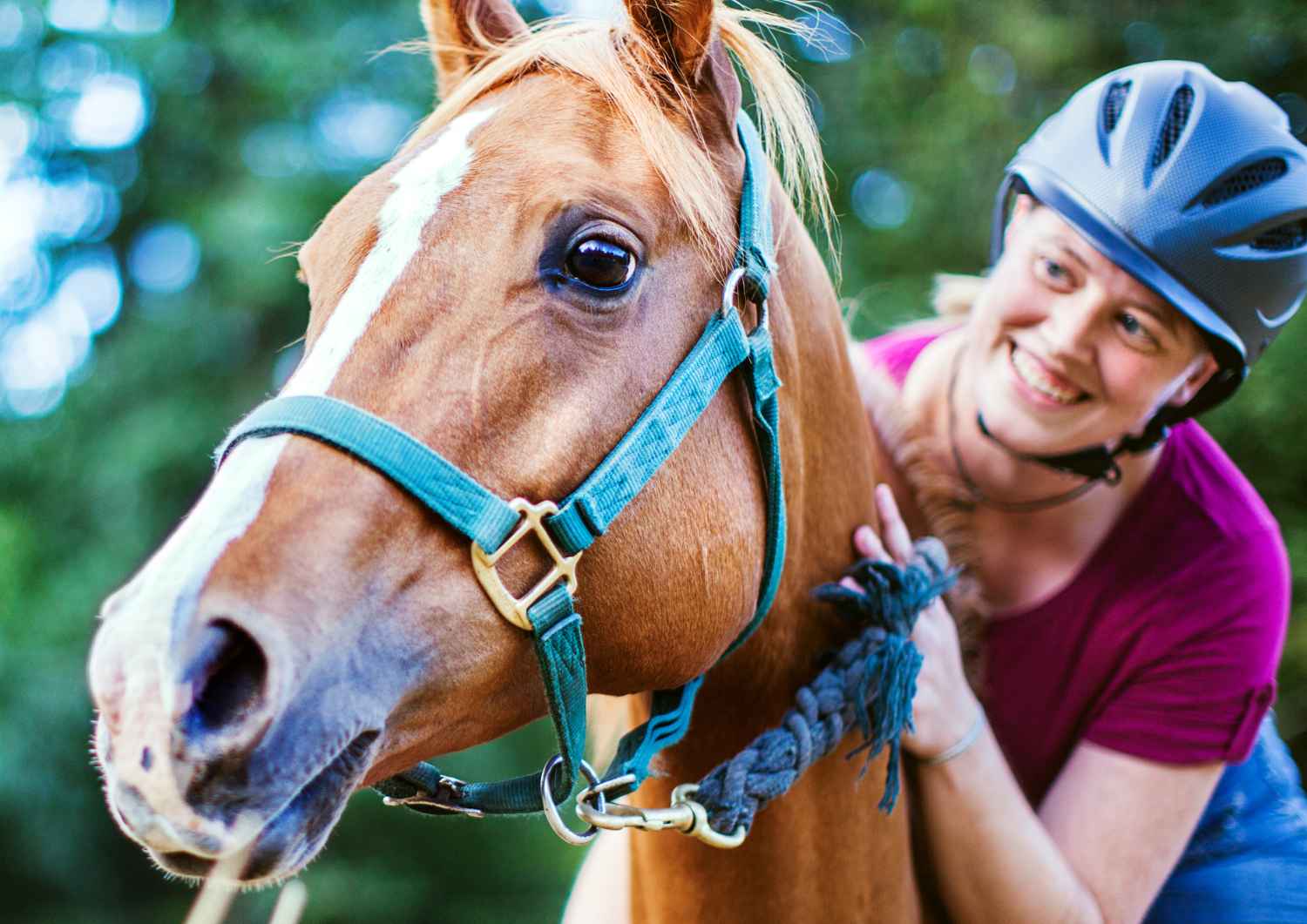 Une cavalière souriante caresse un cheval en laisse dans un cadre naturel pour illustrer la confiance équestre